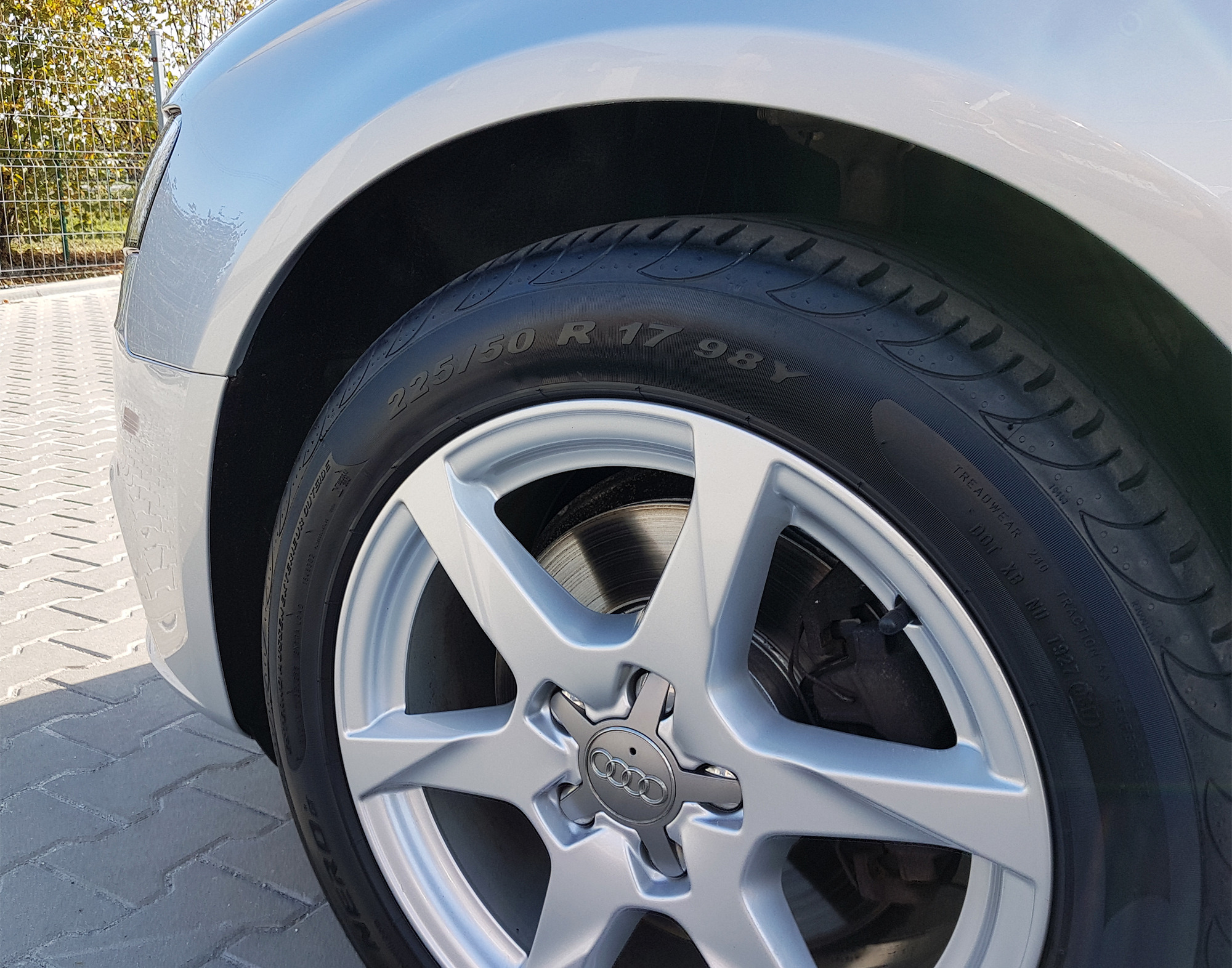 Błyszczące, srebrne felgi aluminiowe z oponą 225/50 R17 na samochodzie Audi, widoczne detale bieżnika opony i zacisk hamulcowy.