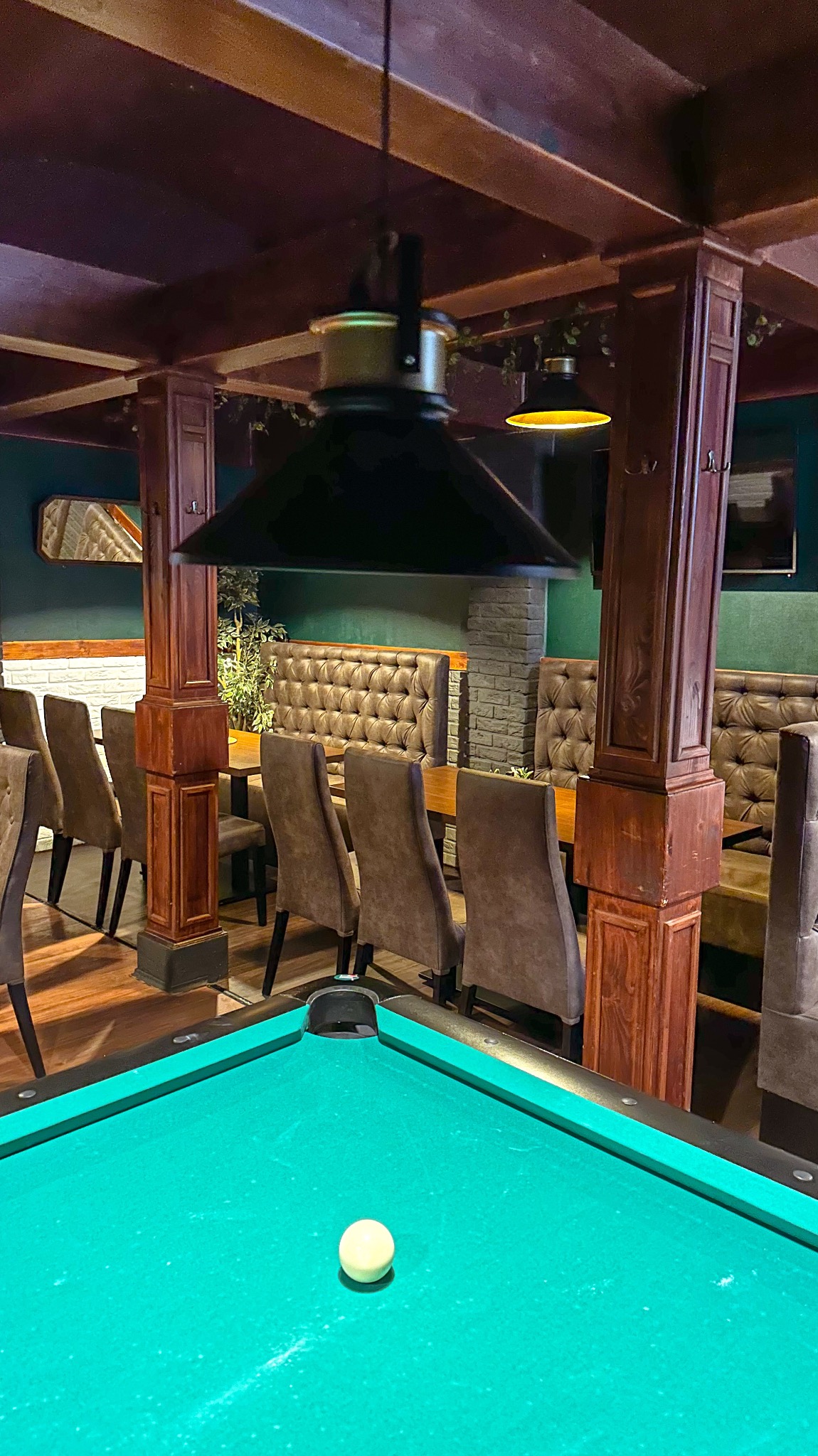 Wnętrze lokalu z zielonym stołem bilardowym, skórzanymi siedziskami w stylu Chesterfield i drewnianymi kolumnami.