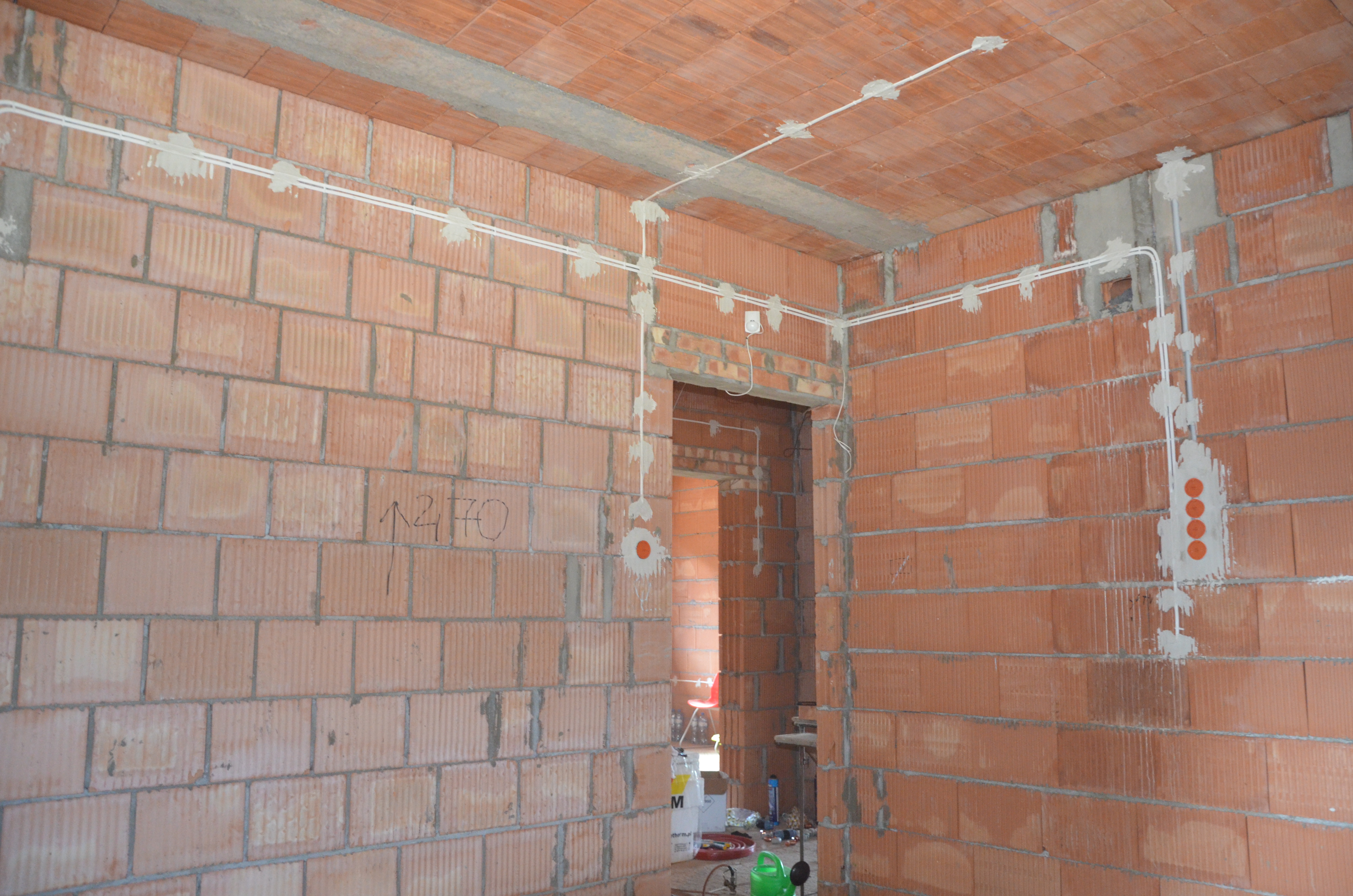 Instalacja elektryczna natynkowa w surowym wnętrzu z cegły, przewody zabezpieczone gipsem, widoczne puszki elektryczne i fragment instalacji podtynkowej.