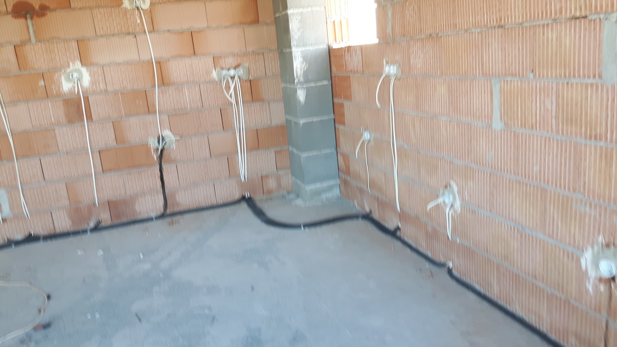 Surowy stan instalacji elektrycznej w nowym budynku: kable w peszlu prowadzone wzdłuż ściany, wystające przewody ze ścian z cegły dziurawki, przygotowane punkty pod gniazdka.