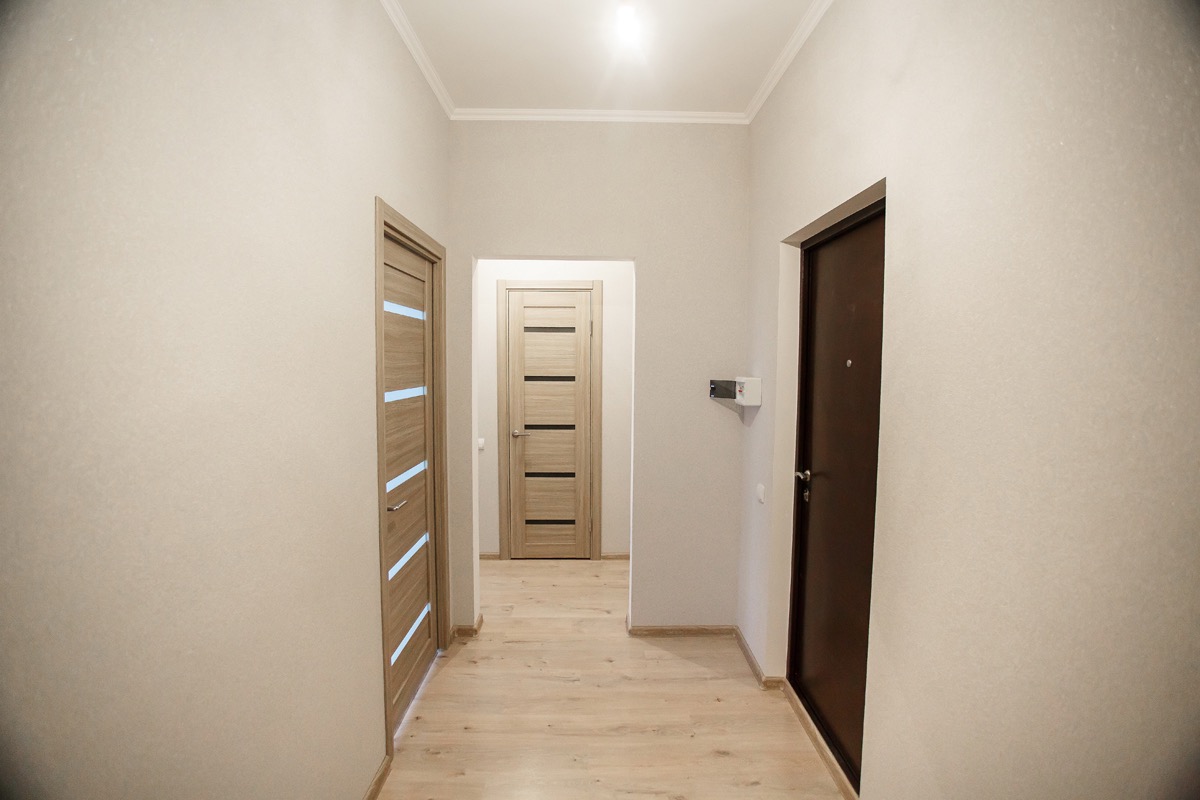Wyremontowany korytarz z trzema drzwiami w odcieniach beżu i brązu, jasna podłoga imitująca drewno, biała listwa przysufitowa, na ścianie zamontowana skrzynka elektryczna.