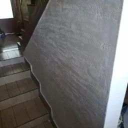 Schody z drewnopodobnymi płytkami i ściana wykończona dekoracyjnym tynkiem w odcieniach szarości, widoczne z boku.