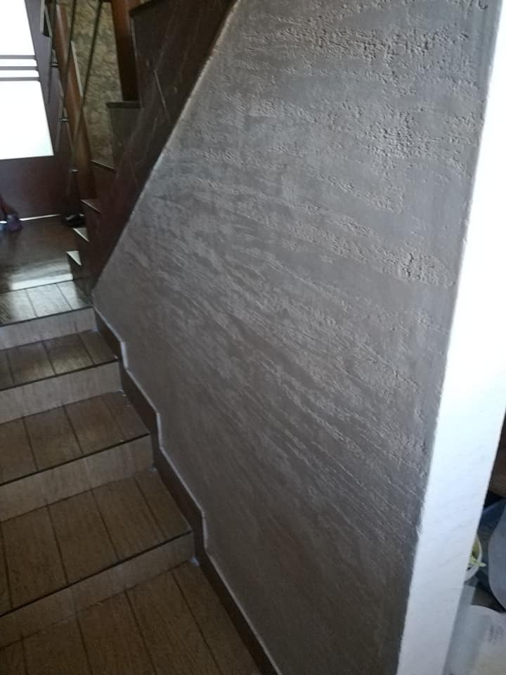 Schody z drewnopodobnymi płytkami i ściana wykończona dekoracyjnym tynkiem w odcieniach szarości, widoczne z boku.