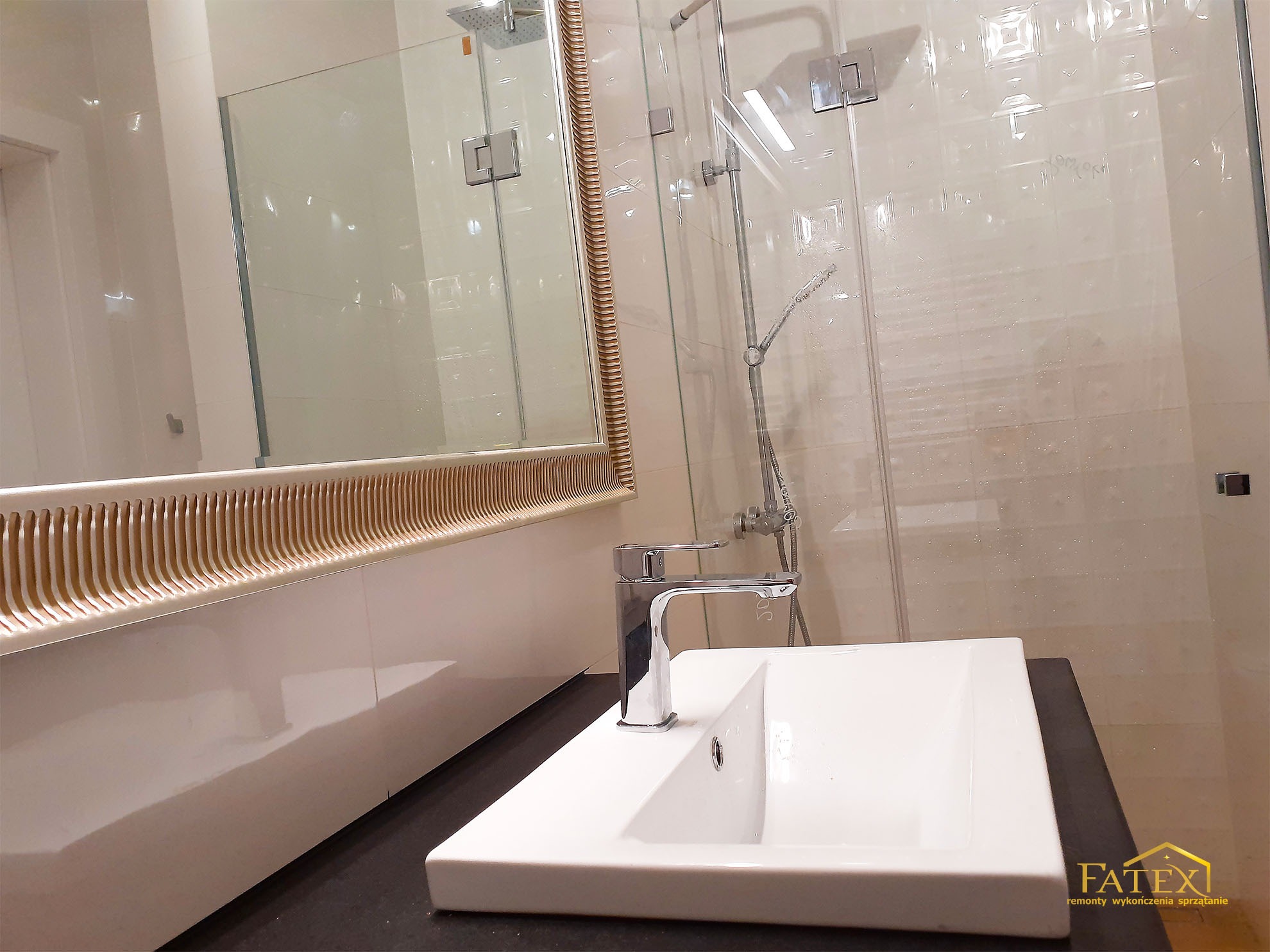 Nowoczesna łazienka z białą umywalką nablatową, chromowaną baterią, lustrem z dekoracyjną ramą i kabiną prysznicową ze szklanymi drzwiami.