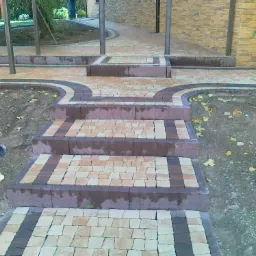 Schody i ścieżka z dwukolorowej kostki brukowej prowadzące do budynku, widoczne liście na ziemi i fragment rynny.