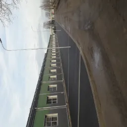 Ukończony parking z kostki brukowej przy budynku przemysłowym, widok z boku, oświetlony przez lampy uliczne. Po prawej stronie widoczna ziemia.