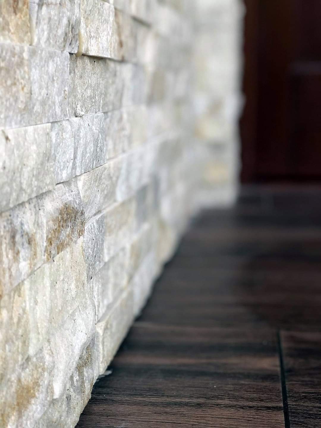 Dekoracyjna ściana z kamienia naturalnego w odcieniach bieli i beżu, ułożona z poziomych płytek, sąsiadująca z ciemną, drewnopodobną podłogą w Szynwałdzie.