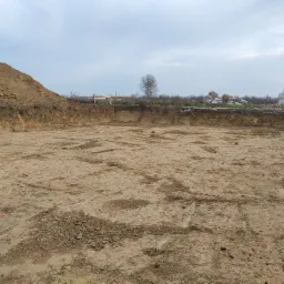 Wykopany dół w ziemi z pryzmą ziemi obok, przygotowany teren pod budowę w pochmurny dzień.