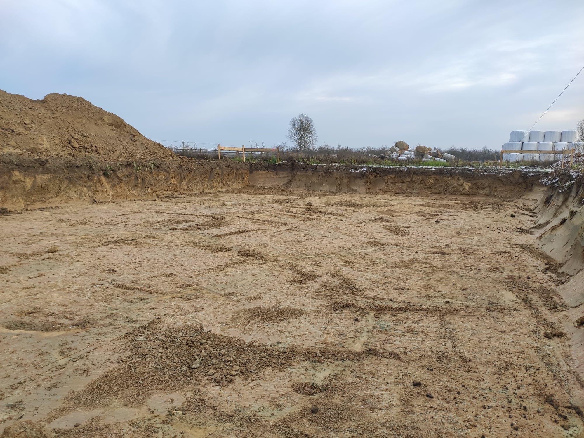 Wykopany dół w ziemi z pryzmą ziemi obok, przygotowany teren pod budowę w pochmurny dzień.