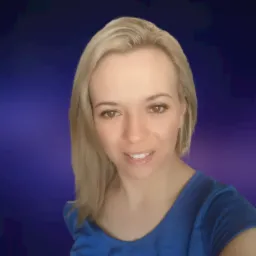 Portret uśmiechniętej blondynki w niebieskiej bluzce na rozmytym, ciemnoniebieskim tle.