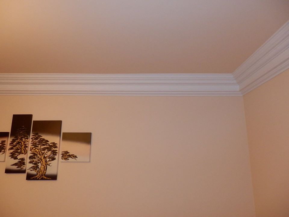 Sypialnia w stylu klasycznym: beżowe ściany, biała listwa gipsowa pod sufitem i obraz z motywem drzew na ścianie.