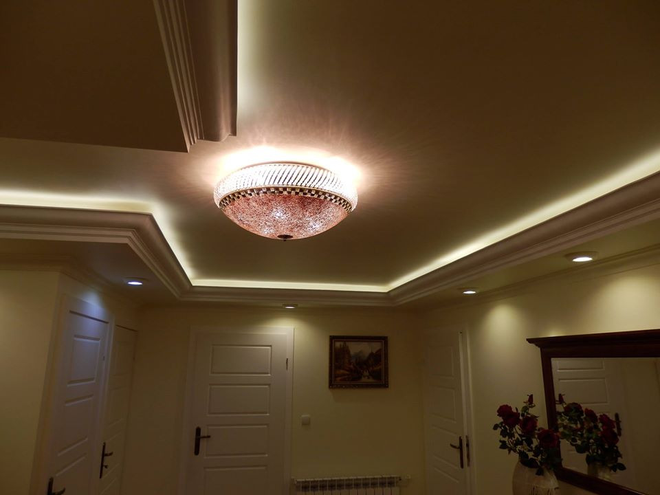 Korytarz w stylu klasycznym z dekoracyjnym oświetleniem sufitowym, listwami gipsowymi i rozetą, uzupełniony o obraz i lustro z bukietem czerwonych róż.