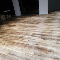 Ułożona podłoga z desek imitujących stare drewno, widok z perspektywy podłogi, w tle kolumny i ciemne pomieszczenie.