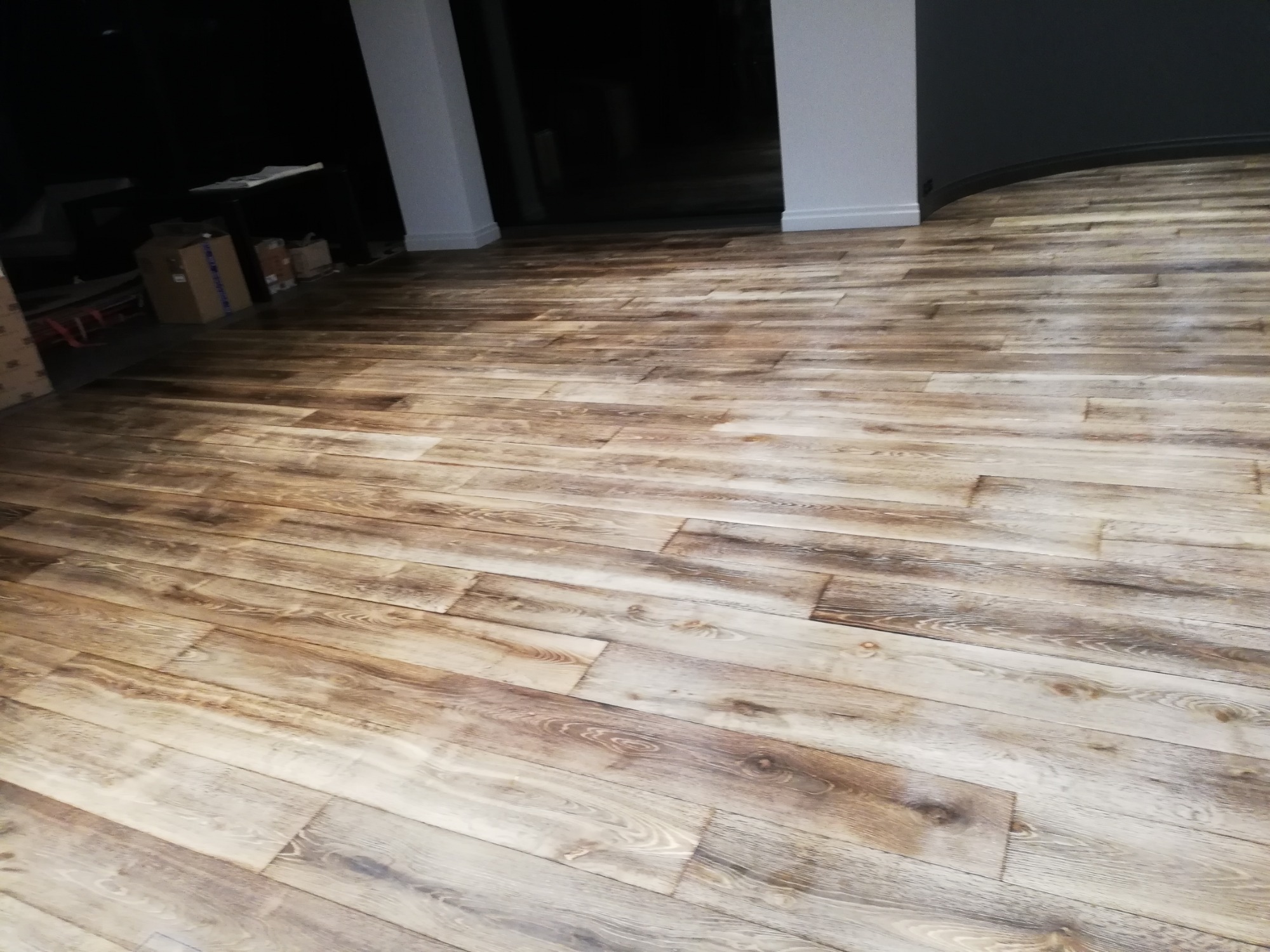 Ułożona podłoga z desek imitujących stare drewno, widok z perspektywy podłogi, w tle kolumny i ciemne pomieszczenie.