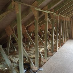 DREW-DOM Andrzej Antecki - Wnętrze poddasza z drewnianą konstrukcją szkieletową i częściowo ułożoną izolacją z wełny mineralnej, widoczne przewody elektryczne w rogu podłogi z płyt OSB.