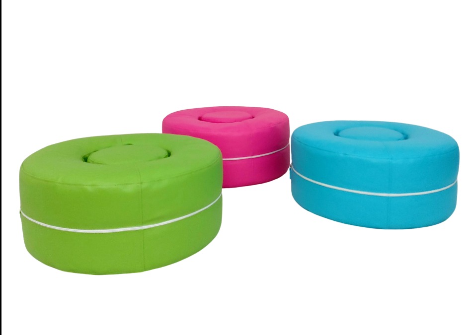 Trzy kolorowe, okrągłe pufy z wgłębieniem na środku, obite tkaniną i wykończone białą lamówką, ustawione na białym tle. Pufy w kolorach: zielonym, różowym i niebieskim.