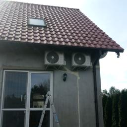 Oskar Klimatyzacja - Dwa klimatyzatory zamontowane na zewnętrznej ścianie domu z czerwonym dachem, widoczna drabina oparta o ścianę i ślady pianki montażowej po instalacji.