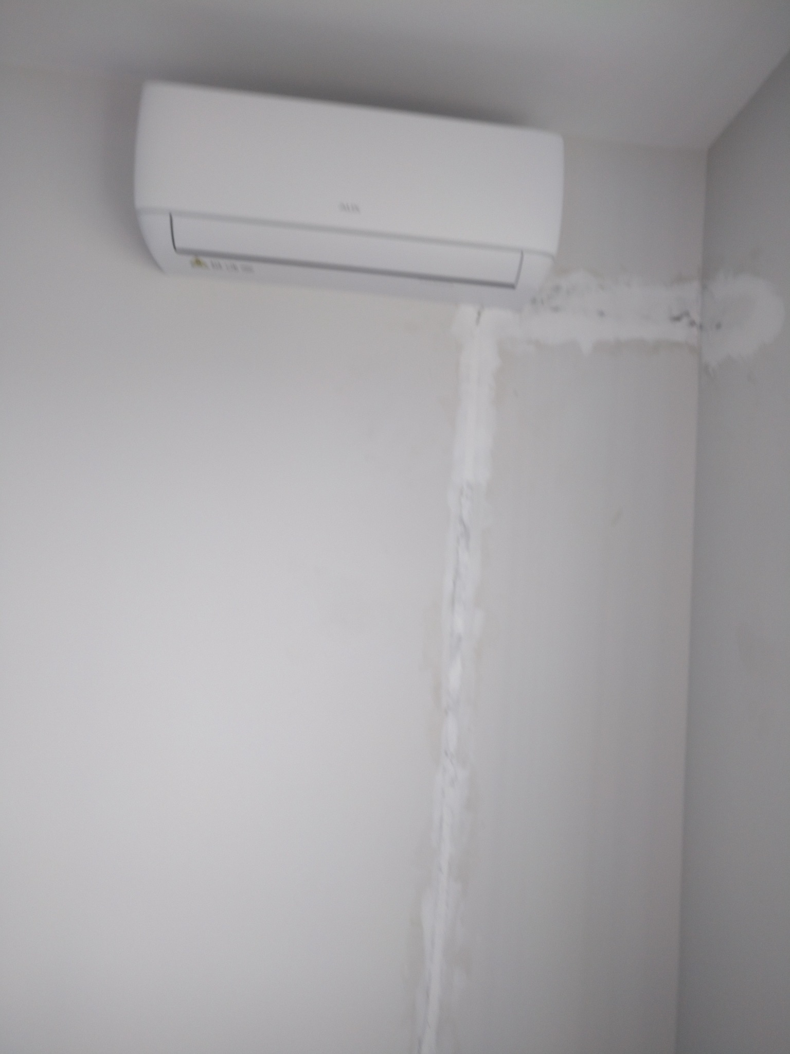 Biały klimatyzator marki AUX zamontowany na ścianie, widoczne ślady po instalacji wymagające wykończenia.