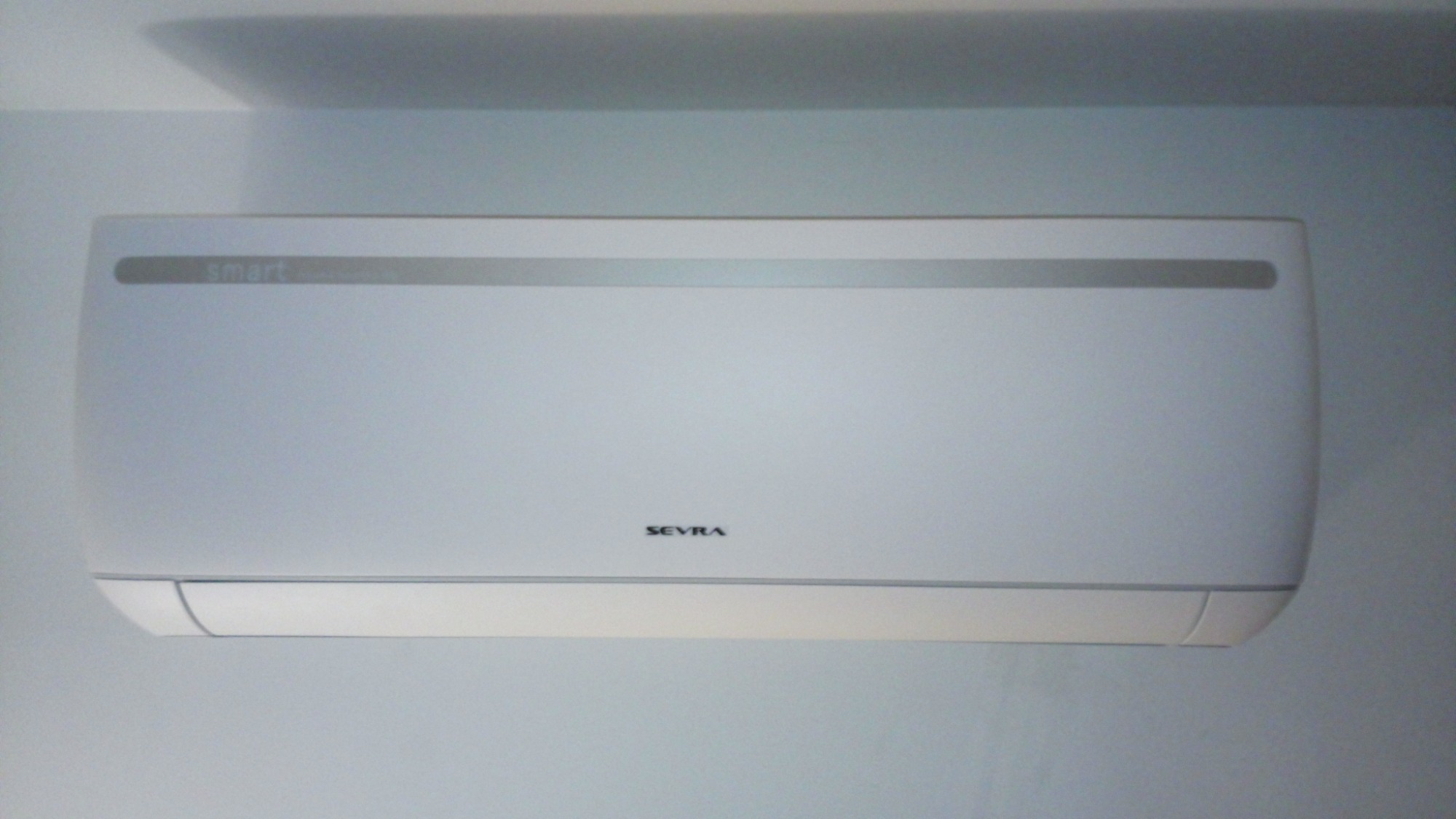 Biała jednostka wewnętrzna klimatyzacji marki Sevra zamontowana na ścianie w pomieszczeniu o jasnych ścianach.