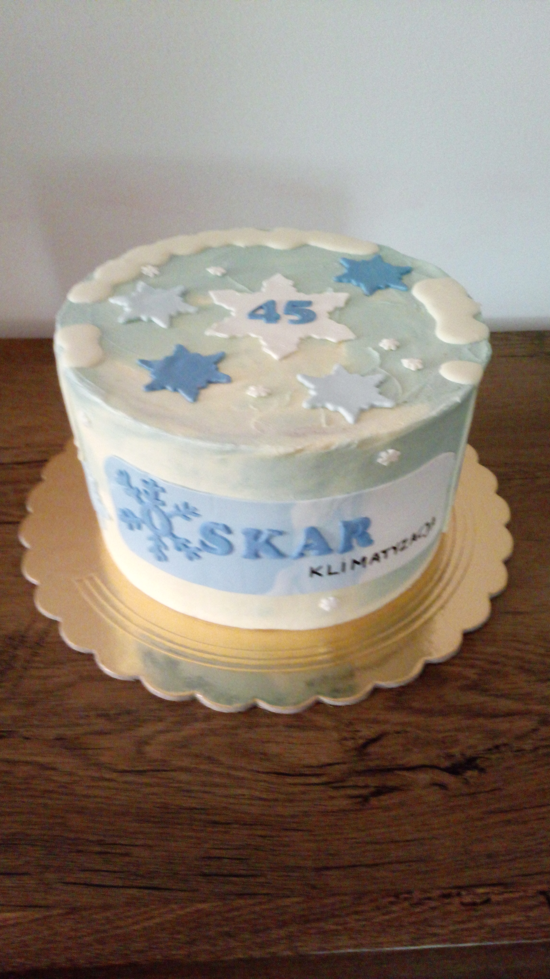 Tort z motywem zimowym, dekorowany gwiazdami, płatkami śniegu i napisem 'SKAR Klimatyzacja' oraz liczbą 45, umieszczony na złotej podkładce.