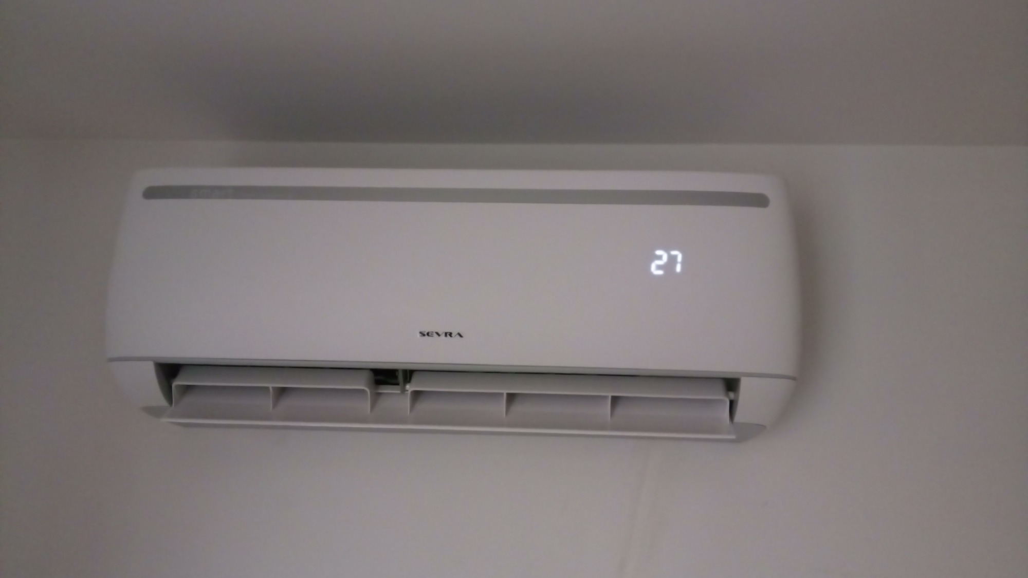 Biała klimatyzacja marki Sevra zamontowana na ścianie w Pęgowie, wyświetlająca temperaturę 27 stopni Celsjusza.