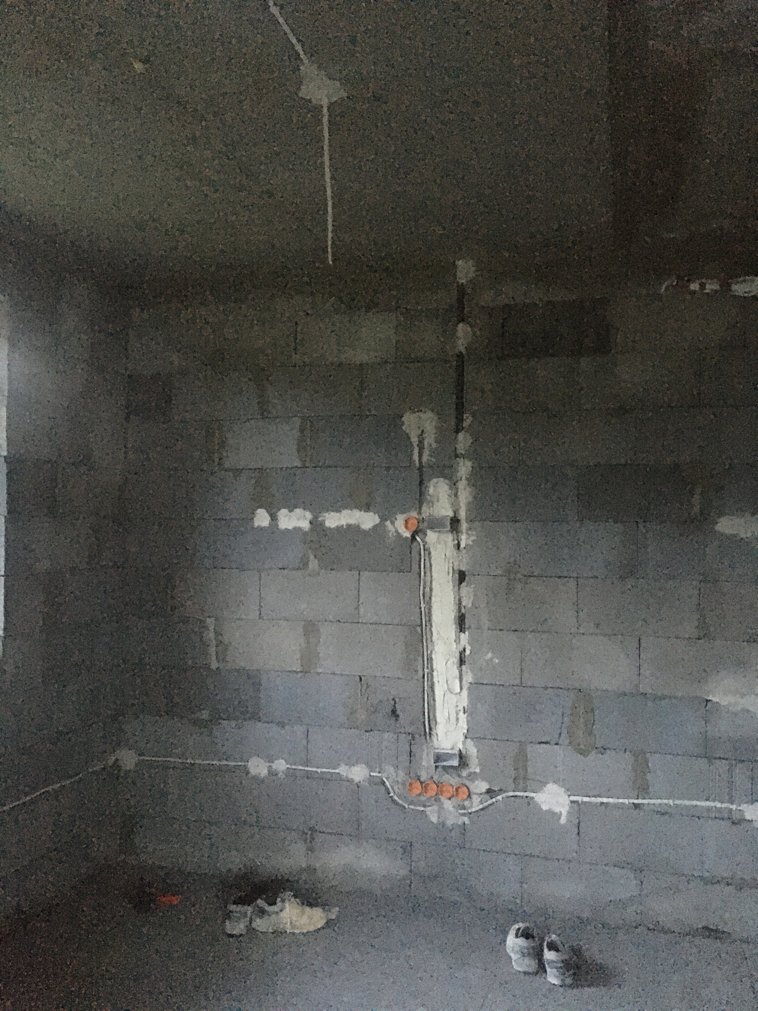 Surowa ściana z betonu komórkowego z widoczną, częściowo zamurowaną instalacją elektryczną w peszlach i puszkach. Widoczne przewody i puszki instalacyjne.