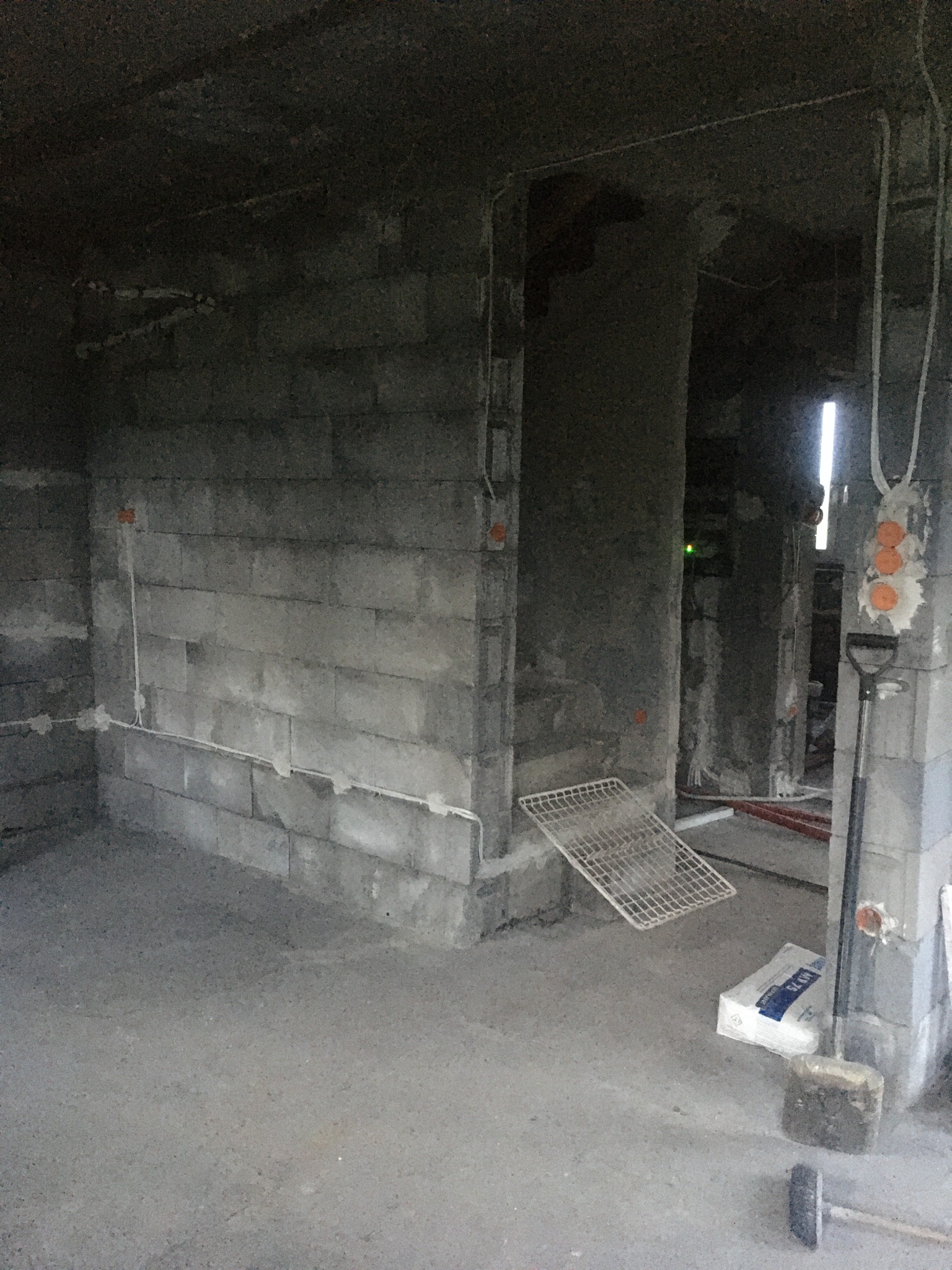 Surowy stan wnętrza z instalacją elektryczną w bruzdach, widoczne kable i puszki. Ściany z betonu komórkowego, podłoga wylewka. W tle przejście do kolejnego pomieszczenia.
