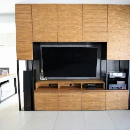 Zabudowa RTV na wymiar z fornirem drewnianym, zintegrowana z szafkami wiszącymi i kolumnami głośnikowymi, widok na jadalnię w tle.