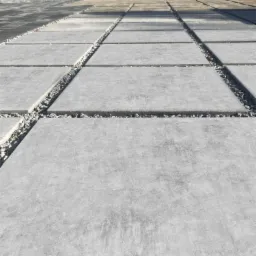 Szara, betonowa nawierzchnia ułożona z prostokątnych płyt, z drobnym grysem wypełniającym szczeliny, widziana pod kątem.