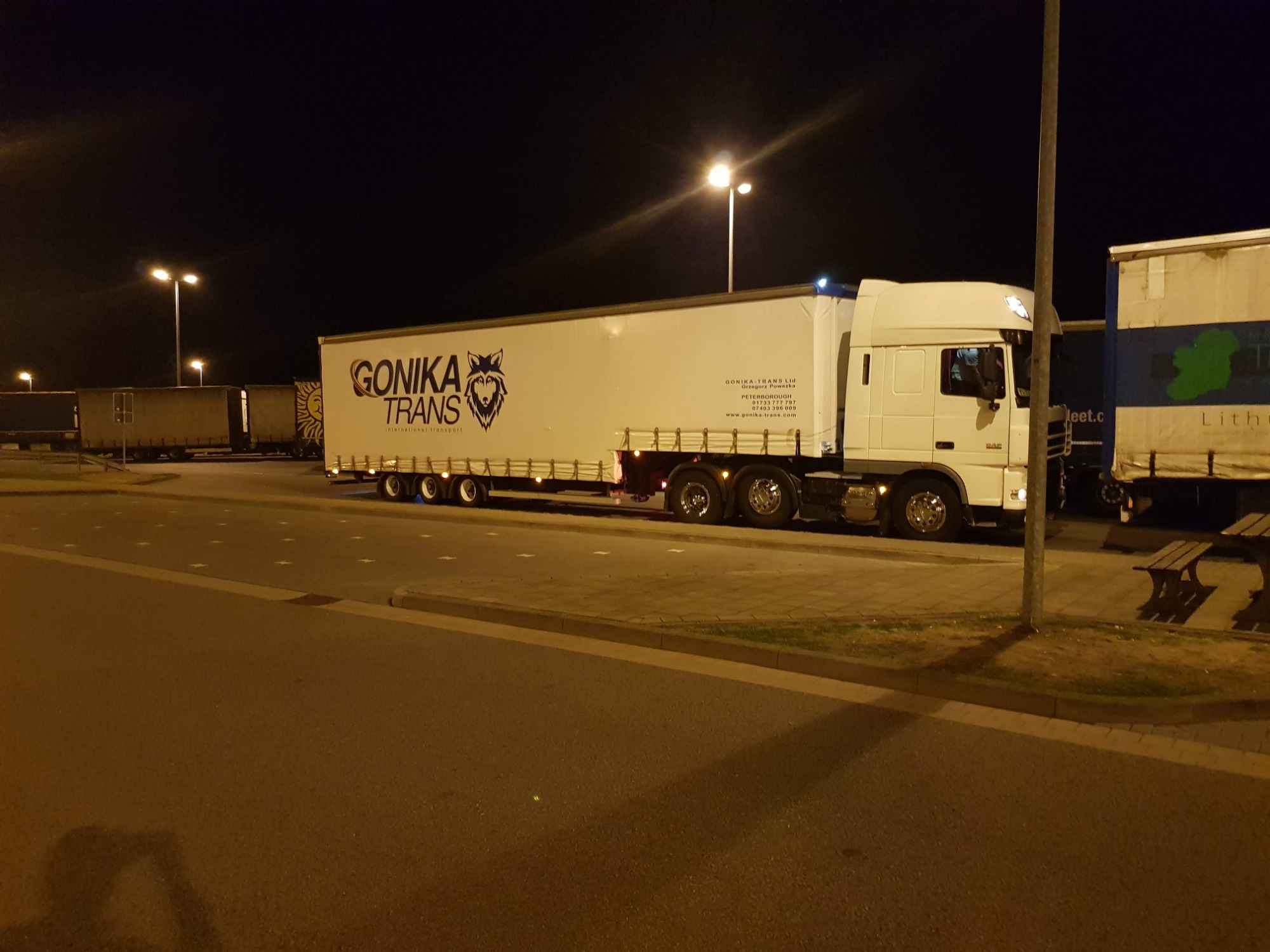 Ciężarówka firmy Gonika Trans zaparkowana nocą na oświetlonym parkingu, widoczne logo firmy z wilkiem na naczepie.