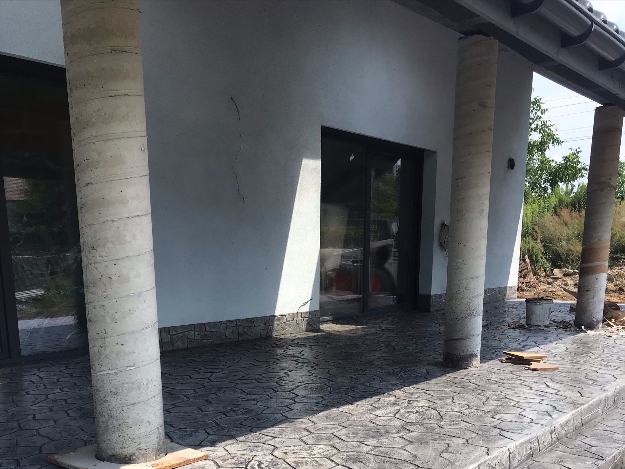 Nowo ułożony, wzorzysty chodnik przy domu z kolumnami, widoczne ślady po pracach budowlanych i wiadro z zaprawą.