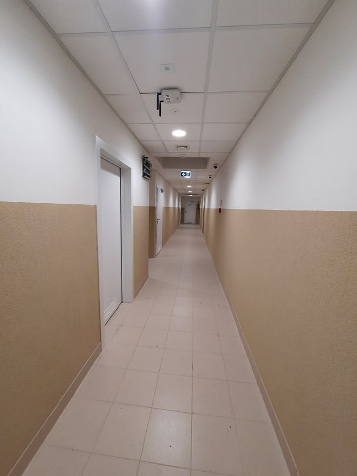 Korytarz biurowy z zamontowanym systemem alarmowym z widoczną centralą alarmową na suficie i kamerami monitoringu.