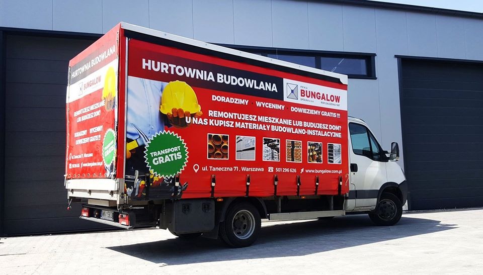 Samochód dostawczy z reklamą hurtowni budowlanej, z widocznym hasłem 'Transport Gratis', zdjęciami materiałów budowlanych i logiem firmy.