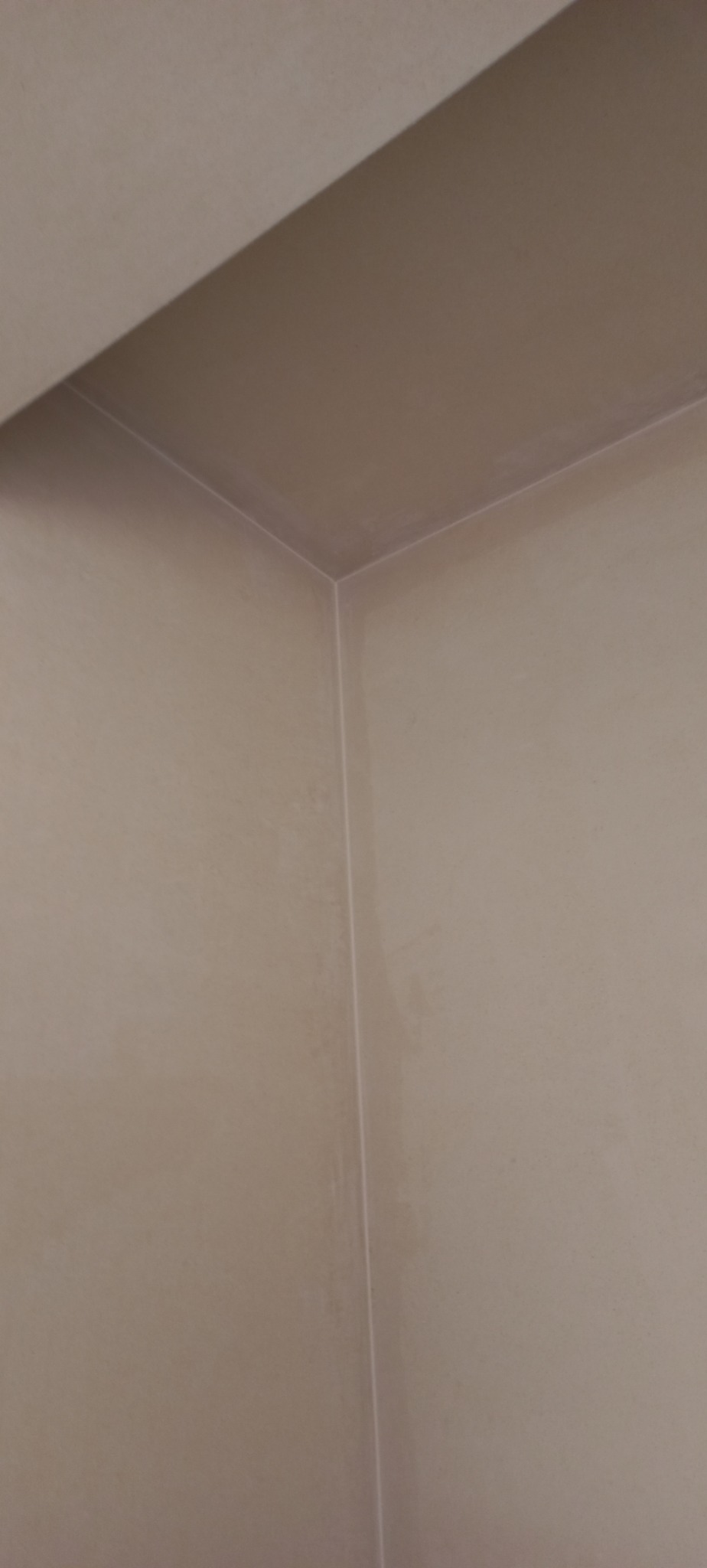 Wnętrze po nałożeniu gładzi gipsowej, widoczny kąt ściany i sufitu, delikatne ślady po szpachlowaniu przed malowaniem.