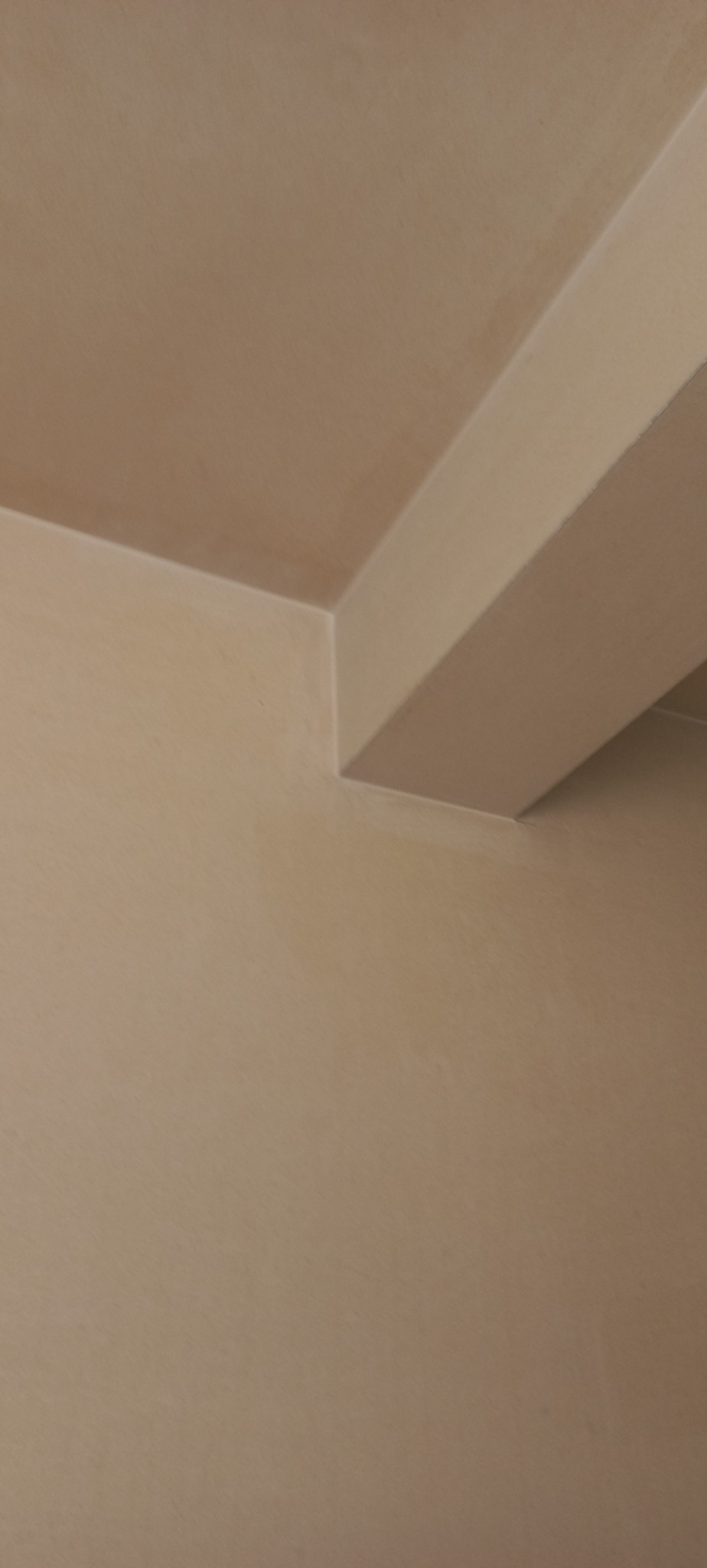 Beżowa ściana i sufit po tynkowaniu maszynowym, widoczna krawędź sufitu i fragment belki konstrukcyjnej