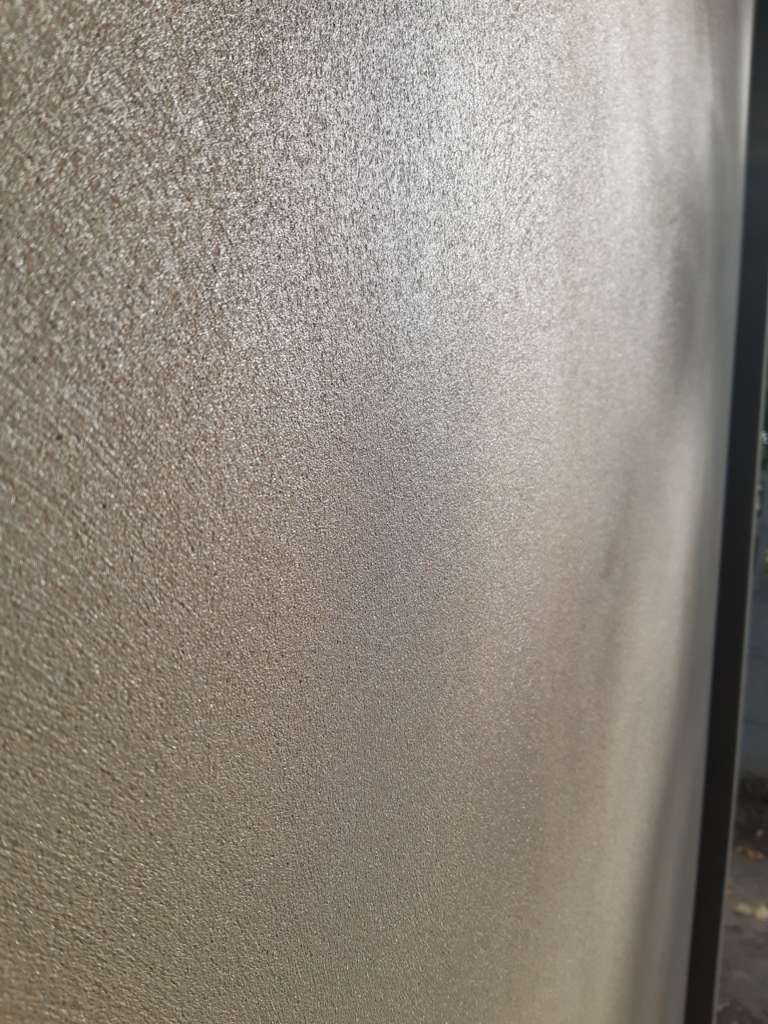 Gładka, beżowa ściana po nałożeniu tynku maszynowego, widoczna faktura i delikatny połysk, ujęcie z boku.