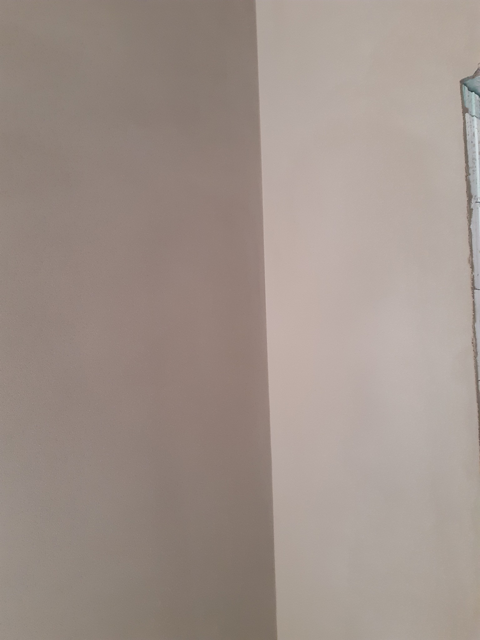 Gładka, beżowa ściana po nałożeniu tynku z widocznym narożnikiem okiennym w stanie surowym.