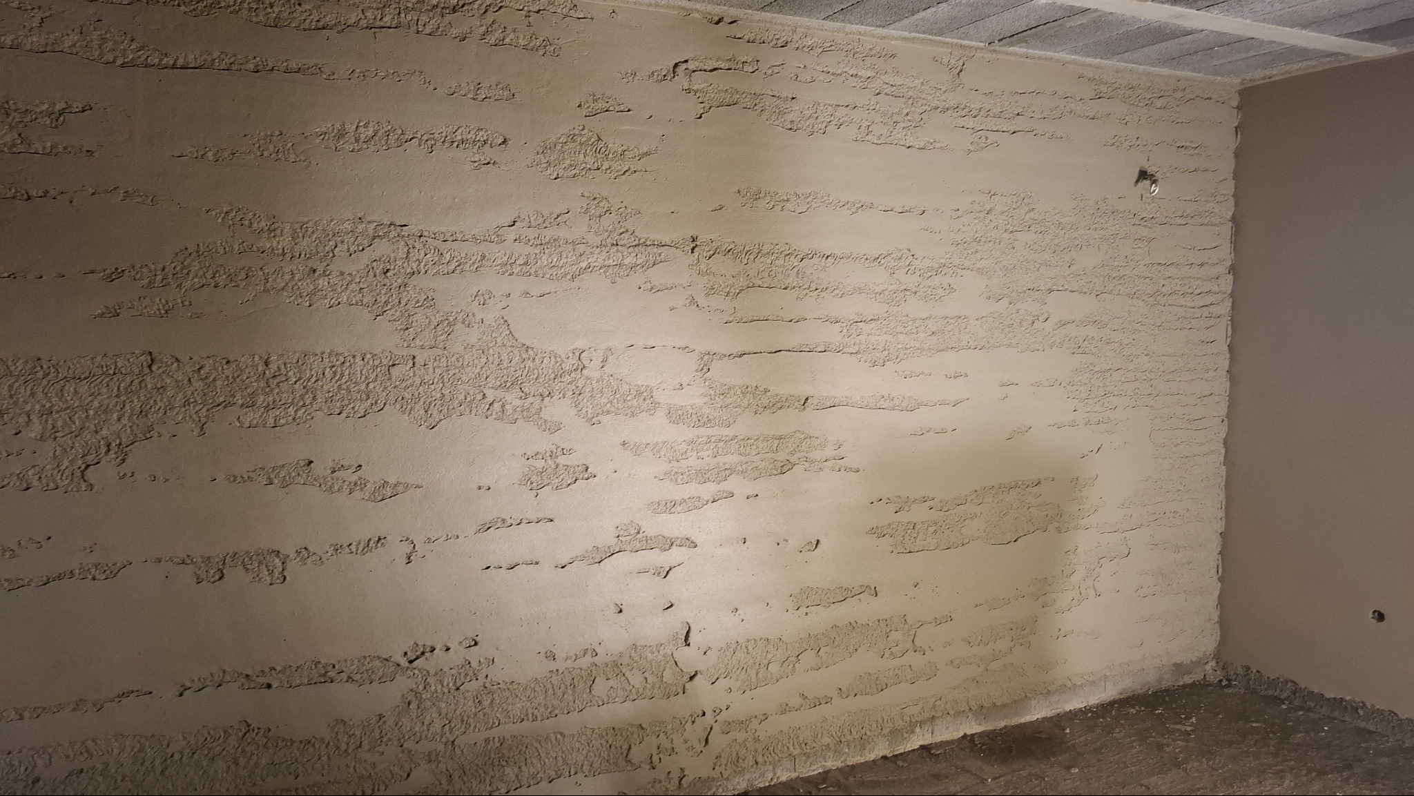 Świeżo nałożony, surowy tynk strukturalny na ścianie wewnętrznej, widoczne nierówności i ślady po narzędziach, jasne oświetlenie boczne podkreśla fakturę.