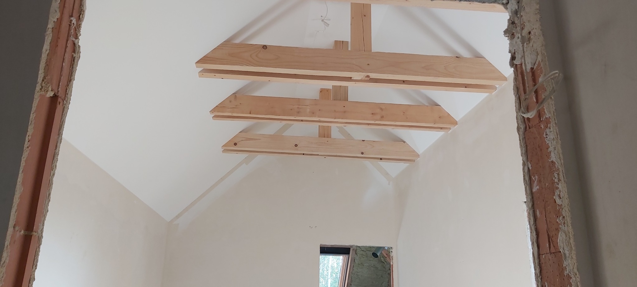 Wnętrze w trakcie remontu z widoczną drewnianą konstrukcją podtrzymującą sufit i ścianami przygotowanymi pod gładzie.
