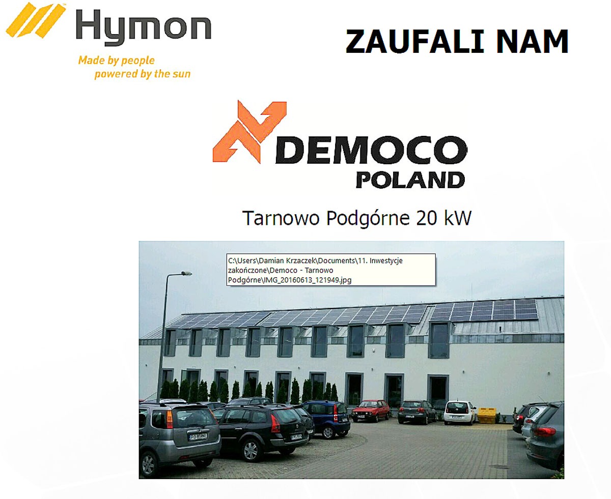 Budynek w Tarnowie Podgórnym z panelami słonecznymi na dachu, logo Democo Poland i Hymon, informacja o mocy 20kW oraz zaparkowane samochody.