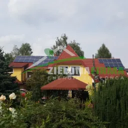 Żółty dom jednorodzinny z panelami słonecznymi na czerwonym dachu, widok z ogrodu z altaną i kwitnącymi różami.