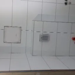 Białe płytki ceramiczne ułożone na ścianie w łazience, widoczne otwory wentylacyjne, rewizja, instalacja podtynkowa WC, fragment podłogi w trakcie prac.