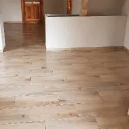 Nowa podłoga z płytek imitujących drewno w jasnej łazience z drewnianymi elementami konstrukcyjnymi pod skosem dachu.