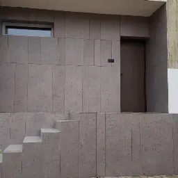 Elewacja budynku z szarymi płytami kamiennymi, schody wejściowe, okno i drzwi wejściowe, widoczne narzędzia i kubki na zewnątrz.