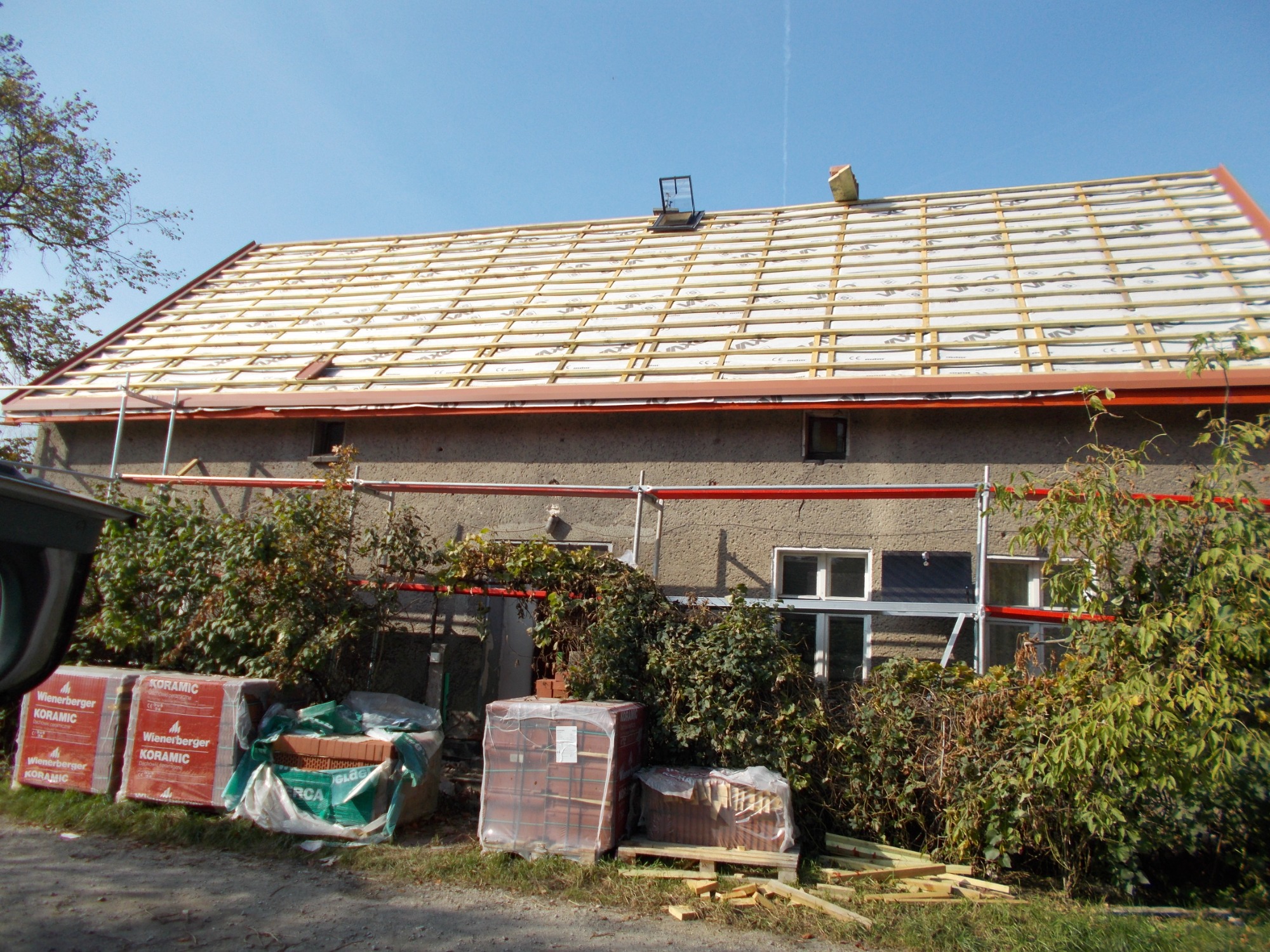 Dom w trakcie wymiany pokrycia dachowego, widoczne przygotowane łaty pod dachówkę oraz cegły KORAMIC na ziemi.