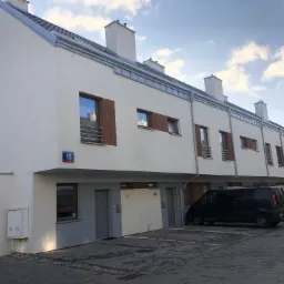 Nowoczesne szeregowe domy z szarym dachem i białymi ścianami, widok z ulicy, numer 15 na budynku, zaparkowane samochody.