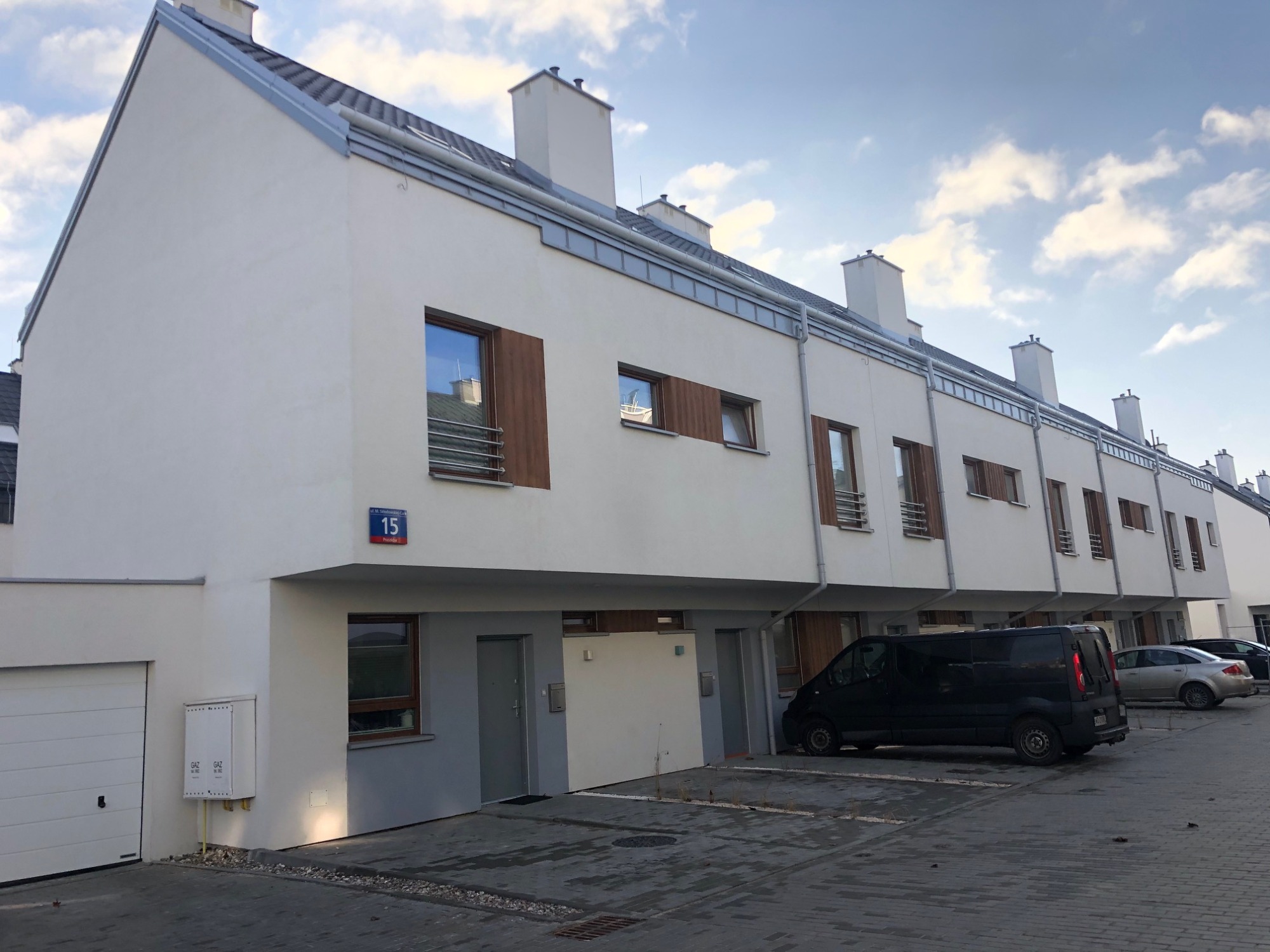 Nowoczesne szeregowe domy z szarym dachem i białymi ścianami, widok z ulicy, numer 15 na budynku, zaparkowane samochody.