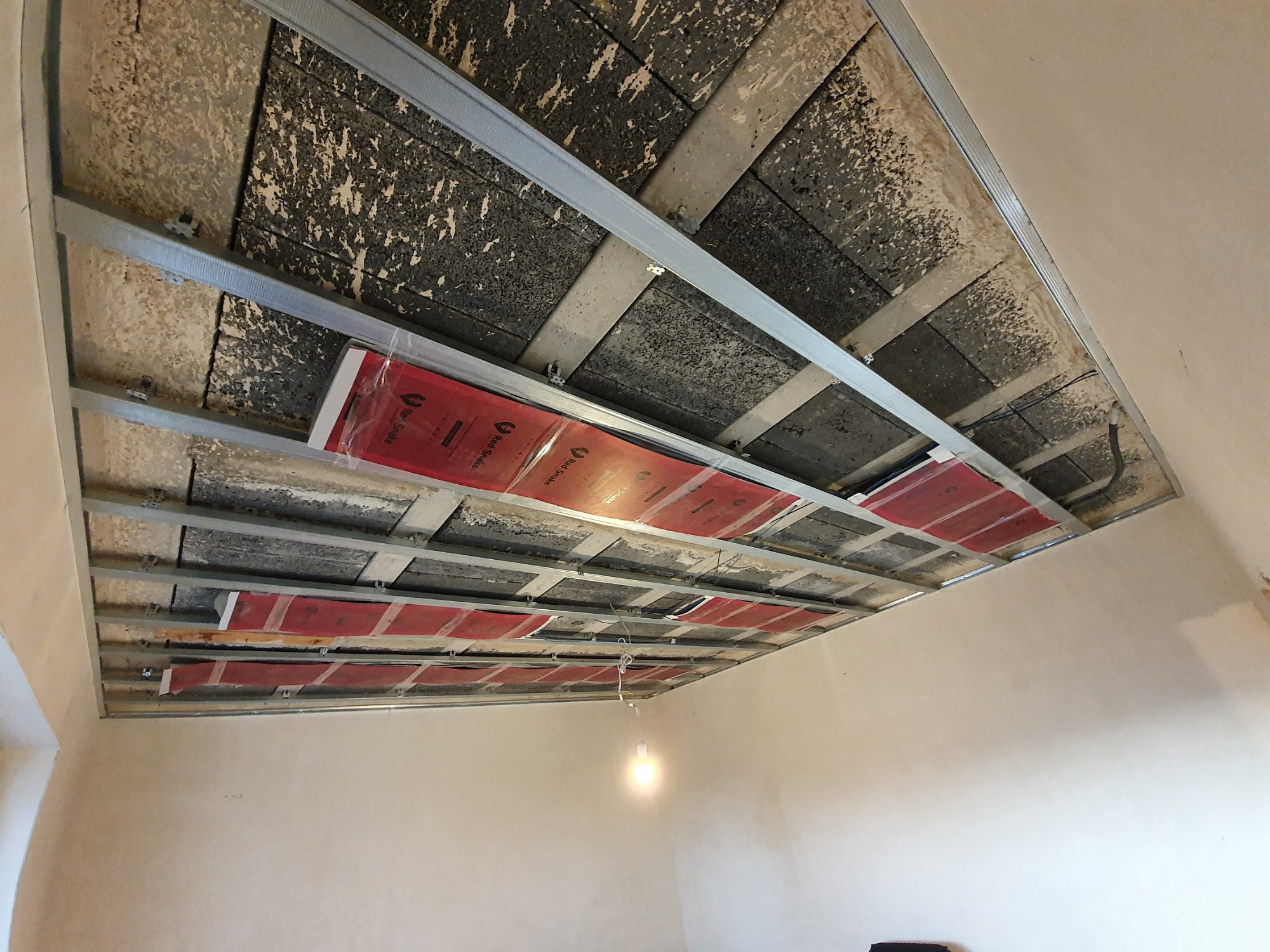 Sufit podwieszany z zamontowaną folią grzewczą Red Snake, widoczne profile metalowe i płyty sufitowe, instalacja w trakcie realizacji.