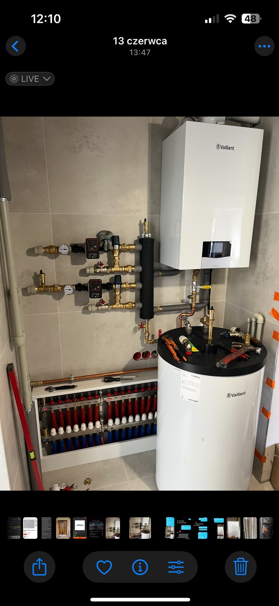 Nowoczesna kotłownia z białym piecem Vaillant, rozdzielaczem ogrzewania podłogowego i kompletną instalacją hydrauliczną na tle beżowych płytek. Widoczne narzędzia.