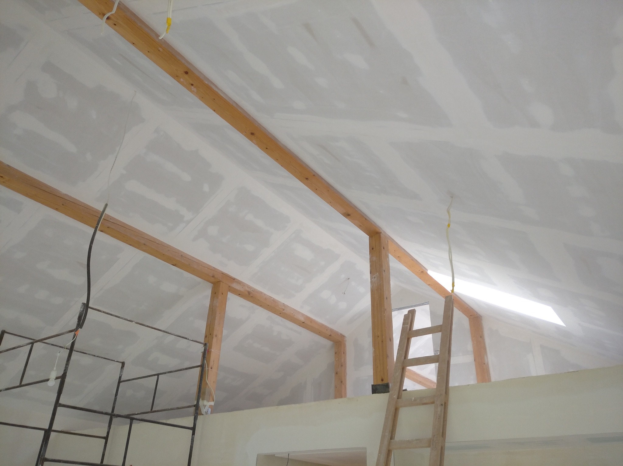 Sufit poddasza z drewnianą konstrukcją, pokryty płytami gipsowo-kartonowymi przed szpachlowaniem, widoczny fragment rusztowania i drabina.